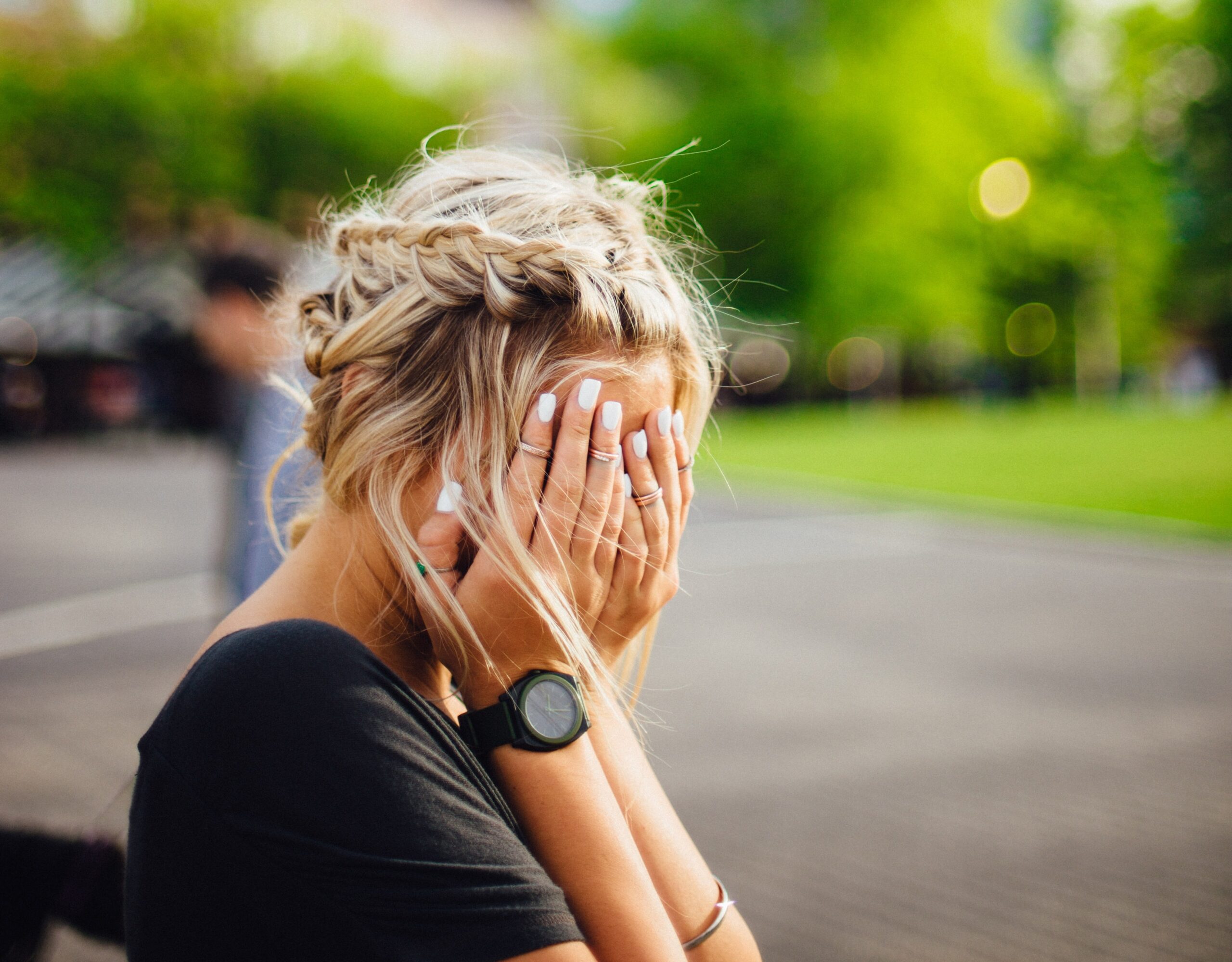 Woman sitting outdoors holding her head in her hands
